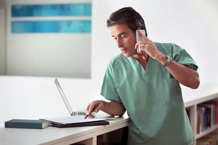Framed Print : Hispanic Male doctor in his home practicing Telemedicine, talking on cell phone and taking notes Framed Print : Hispanic Male doctor in his home practicing Telemedicine, talking on cell phone and taking notes