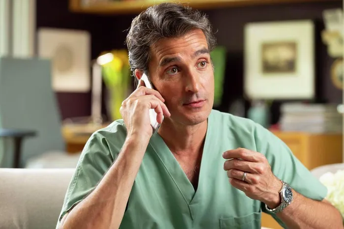 Framed Print : Hispanic Male doctor practicing tele-medicine from his home office, Talking to patient on cell phone