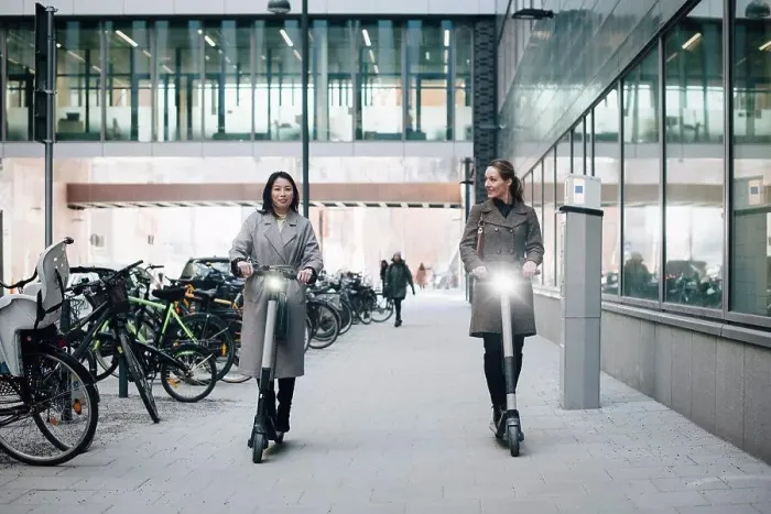 Framed Print : Full length of confident female colleagues riding electric push scooter on footpath by building in city