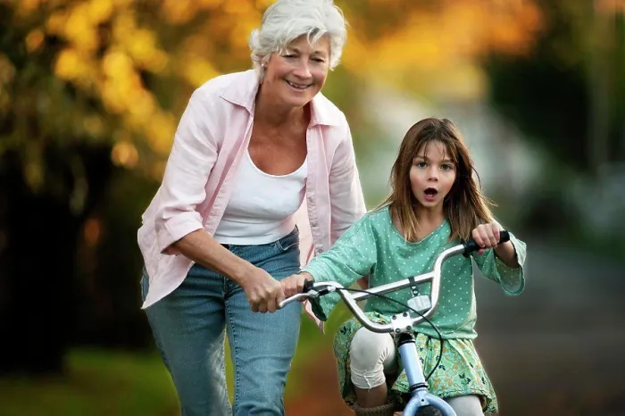 Framed Print : Little girl learning to ride her bicycle with the help of her grandmother Framed Print : Little girl learning to ride her bicycle with the help of her grandmother