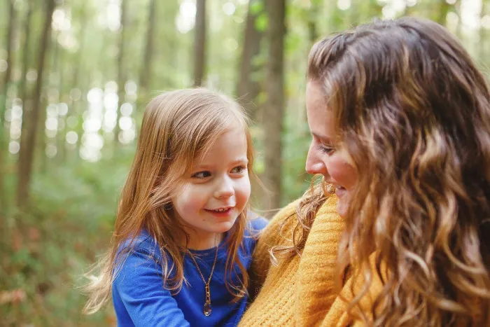 Framed Print : A little girl snuggles in her mother's arms as they smile together Framed Print : A little girl snuggles in her mother's arms as they smile together