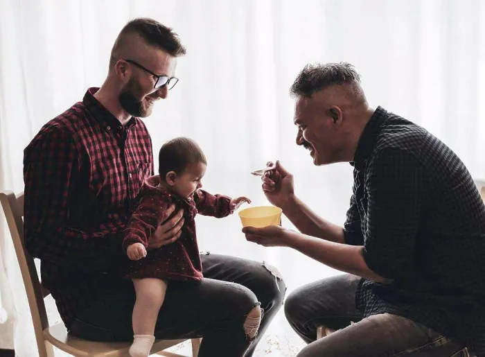 Framed Print : Male gay couple with adopted baby girl at home - Two handsome dads feed the baby girl on kitchen - Male babysitters Framed Print : Male gay couple with adopted baby girl at home - Two handsome dads feed the baby girl on kitchen - Male babysitters
