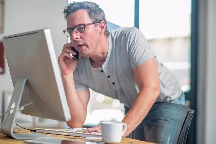 Framed Print : Man at computer using smartphone to make telephone call Framed Print : Man at computer using smartphone to make telephone call