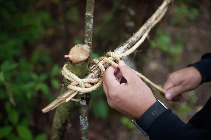 Framed Print : Man ties sticks together with twine to make tree fort