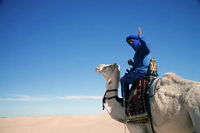 Framed Print : A man wearing a traditional blue robe and headscarf, waves from his white camel Framed Print : A man wearing a traditional blue robe and headscarf, waves from his white camel