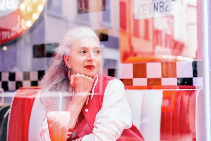 Framed Print : Mature woman in baseball jacket looking through window from 1950's diner