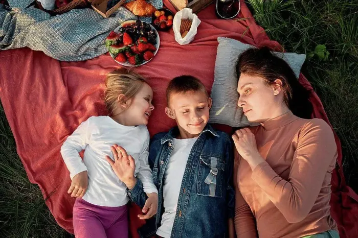 Framed Print : Mother looking at children lying on picnic blanket in field
