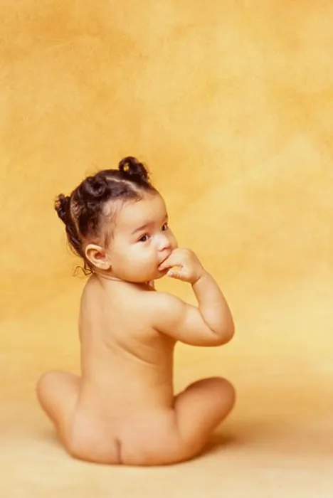 Framed Print : Naked African-American baby sits in a studio with her back to the camera and looks over her shoulder