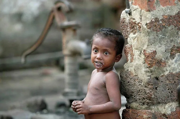 Framed Print : A naked child standing against a wall with a water hand pump in the background; Gopinathpur Village, India Framed Print : A naked child standing against a wall with a water hand pump in the background; Gopinathpur Village, India