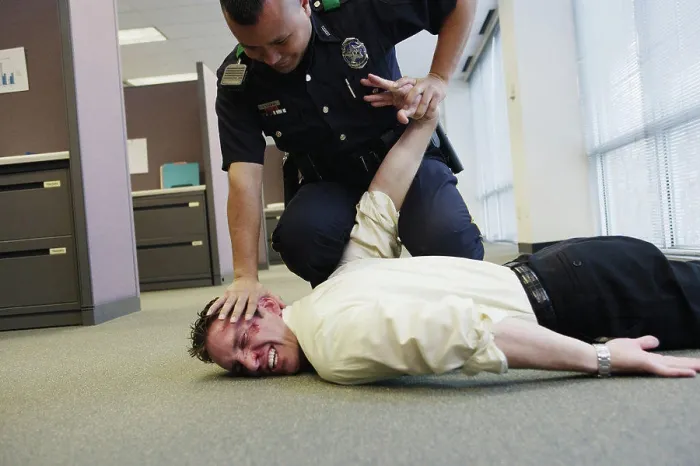 Framed Print : Police officer holding beat up businessman on floor in office Framed Print : Police officer holding beat up businessman on floor in office