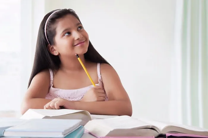 Framed Print : Portrait of smiling cute girl thinking at desk with books Framed Print : Portrait of smiling cute girl thinking at desk with books
