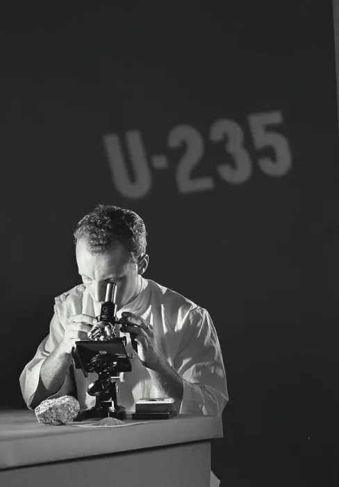 Framed Print : Scientist looking through microscope with U-235 (Uranium Isotope) being projected on the wall Framed Print : Scientist looking through microscope with U-235 (Uranium Isotope) being projected on the wall