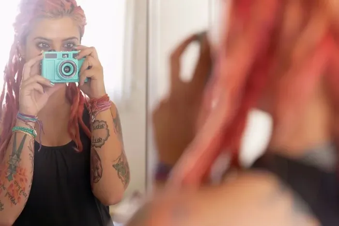 Framed Print : Over shoulder mirror view of young woman with pink dreadlocks taking selfie Framed Print : Over shoulder mirror view of young woman with pink dreadlocks taking selfie