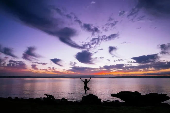Framed Print : Silhouette of a woman performing a yoga pose on a rock by the waterside at sunset