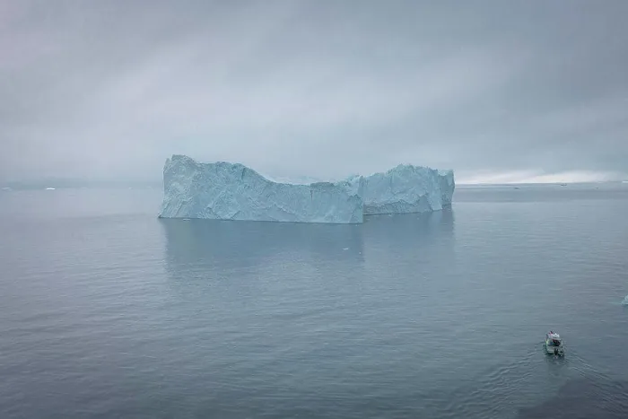 Framed Print : small boat sailing in front of extreme icebergs from aerial view