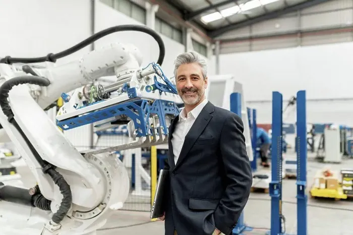 Framed Print : Smiling businessman holding laptop standing by robotic arm in factory Framed Print : Smiling businessman holding laptop standing by robotic arm in factory
