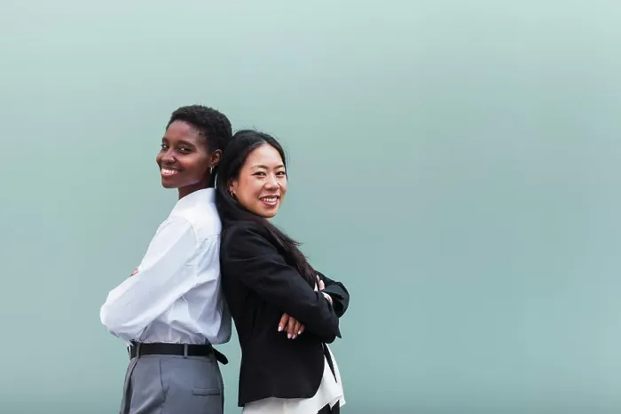 Framed Print : Smiling businesswomen with arms crossed standing back to back in front of blue wall Framed Print : Smiling businesswomen with arms crossed standing back to back in front of blue wall