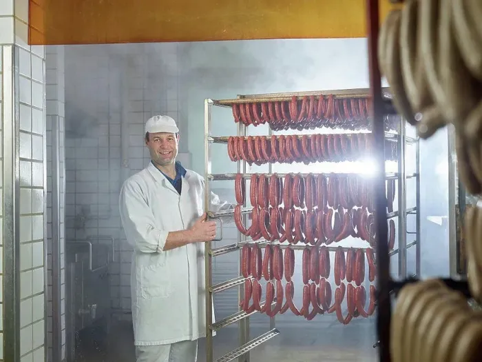 Framed Print : Smiling butcher standing by arranged sausages in smokehouse Framed Print : Smiling butcher standing by arranged sausages in smokehouse