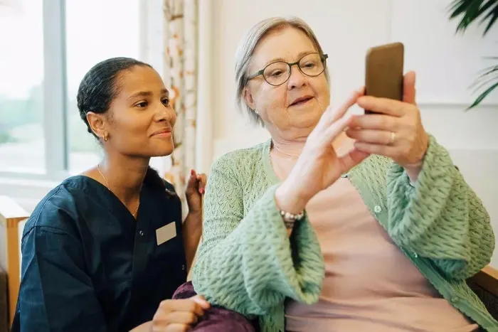 Framed Print : Smiling female caretaker looking at senior woman using mobile phone in nursing home Framed Print : Smiling female caretaker looking at senior woman using mobile phone in nursing home