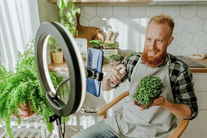 Framed Print : Smiling man spraying water on microgreens sitting in front of smart phone