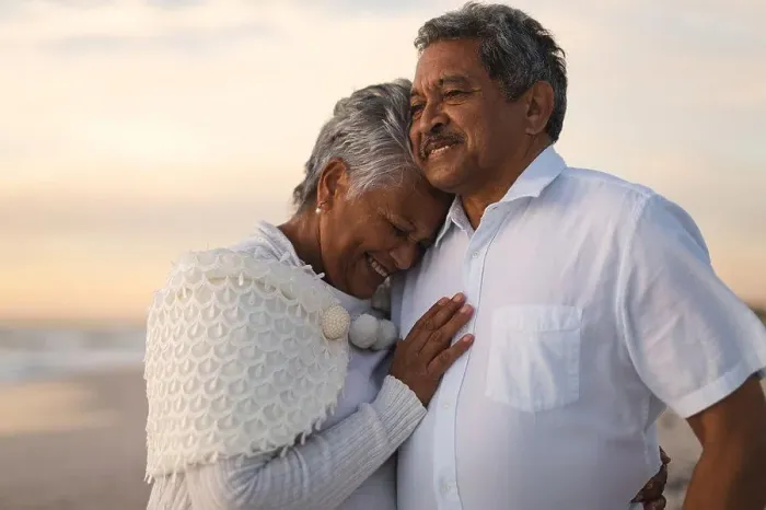 Framed Print : Smiling senior biracial woman embracing man looking away while standing at beach during sunset