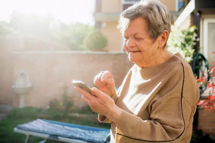 Framed Print : Smiling senior woman using smart phone while standing at backyard during sunny day Framed Print : Smiling senior woman using smart phone while standing at backyard during sunny day