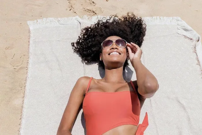 Framed Print : Smiling young woman with curly hair wearing sunglasses while lying on beach towel Framed Print : Smiling young woman with curly hair wearing sunglasses while lying on beach towel