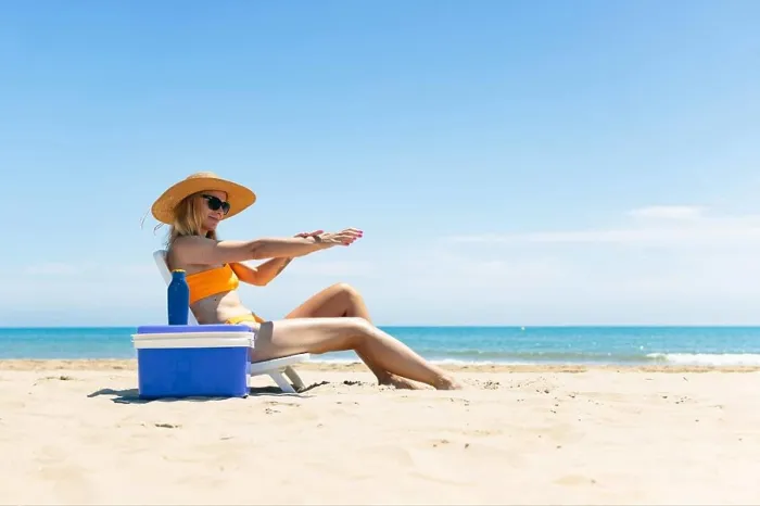 Framed Print : a tanned girl in a swimsuit, hat and glasses sits on a sun lounger smears sunscreen on her hands