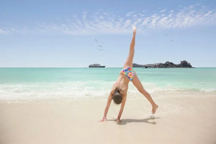 Framed Print : Teenage girl doing a cartwheel on the beach, cruise ship in ocean in background, Galapagos Islands