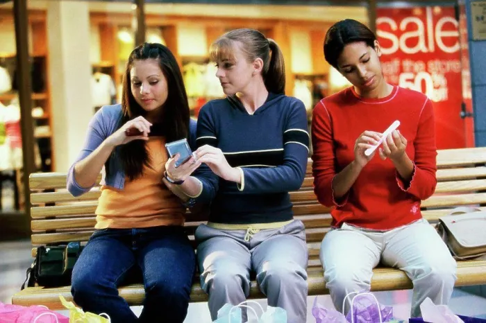 Framed Print : Three teenage girls sitting on a bench in a shopping mall applying make-up