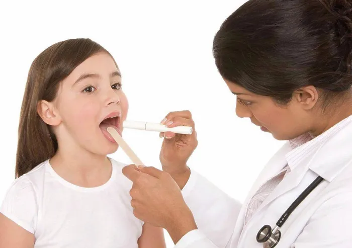 Framed Print : Throat examination. Paediatrician using a tongue depressor and a penlight to examine a girl´s throat