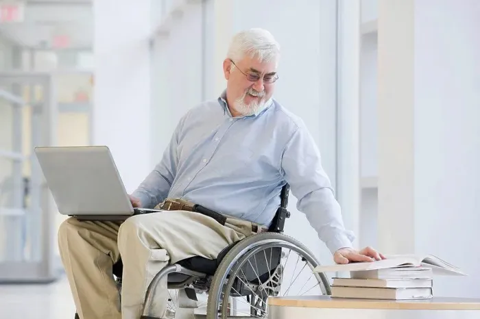 Framed Print : University professor with Muscular Dystrophy reading a book and using a laptop Framed Print : University professor with Muscular Dystrophy reading a book and using a laptop