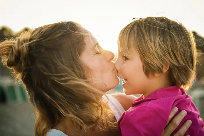 Framed Print : Side view of laughing woman carrying cheerful playful son on hands while kissing his nose on beach in sunset