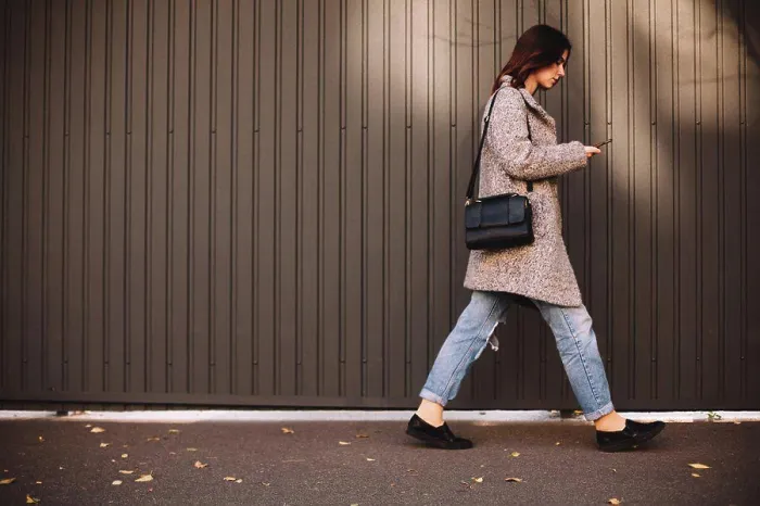 Framed Print : Side view of non-binary woman using smart phone walking against wall Framed Print : Side view of non-binary woman using smart phone walking against wall
