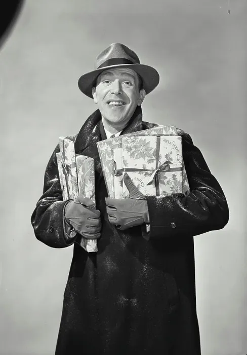 Framed Print : Vintage Photograph. Smiling man wearing hat and winter coat dusted with snow holding wrapped holiday presents