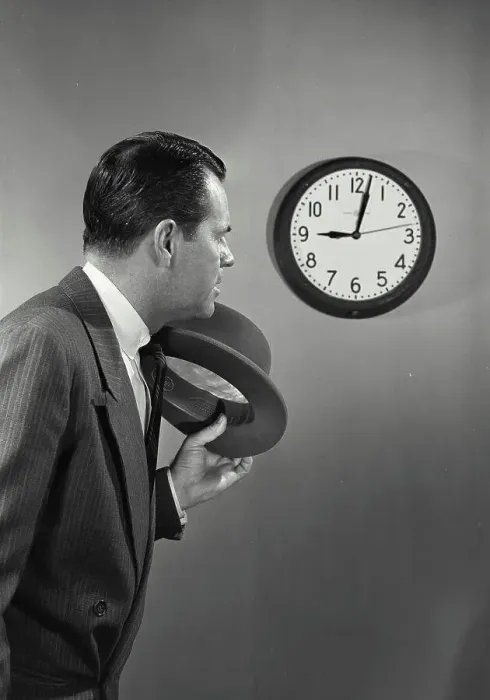 Framed Print : Vintage photograph. Man with dark hair and suit holding hat standing next to wall clock
