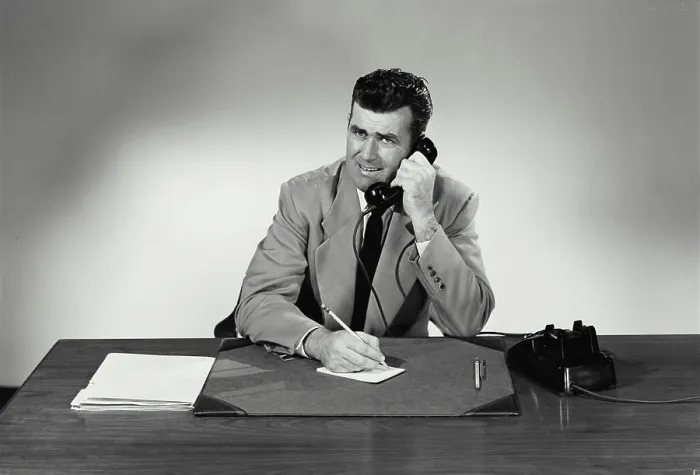 Framed Print : Vintage Photograph. Man sits at desk taking notes he smiles with a concerned look on his face he talks on phone Framed Print : Vintage Photograph. Man sits at desk taking notes he smiles with a concerned look on his face he talks on phone