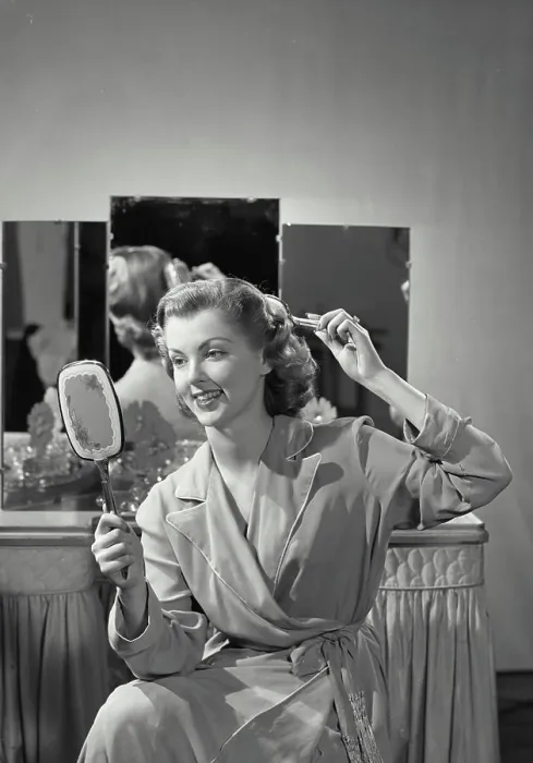 Framed Print : Vintage Photograph. Woman wearing robe combing hair holding up mirror with vanity table in background