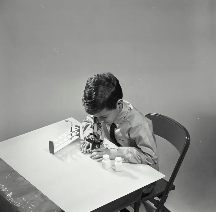 Framed Print : Vintage Photograph. Young boy looking through microscope on table against white backdrop Framed Print : Vintage Photograph. Young boy looking through microscope on table against white backdrop