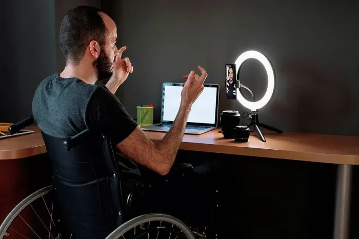 Framed Print : Vlogger filming through mobile phone with circular strobe tripod while sitting on wheelchair at studio Framed Print : Vlogger filming through mobile phone with circular strobe tripod while sitting on wheelchair at studio