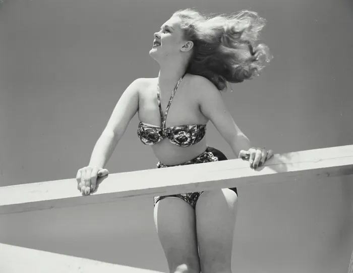 Framed Print : Woman in bikini leaning over railing of deck with hair blowing in wind