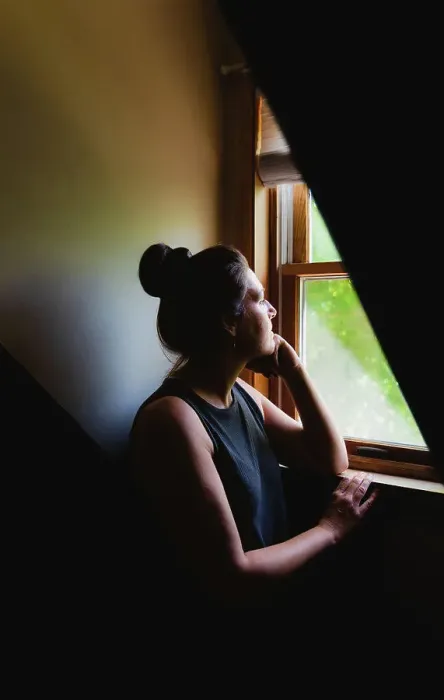 Framed Print : Woman looking out of a window in a dark room in the daytime Framed Print : Woman looking out of a window in a dark room in the daytime