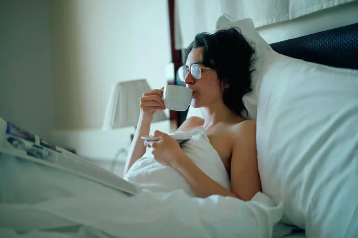 Framed Print : A woman relaxes in bed with a cup of coffee and a newspaper in a cozy bedroom setting Framed Print : A woman relaxes in bed with a cup of coffee and a newspaper in a cozy bedroom setting