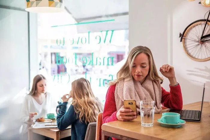 Framed Print : Woman sitting in cafe, looking at smartphone, laptop in front of her Framed Print : Woman sitting in cafe, looking at smartphone, laptop in front of her