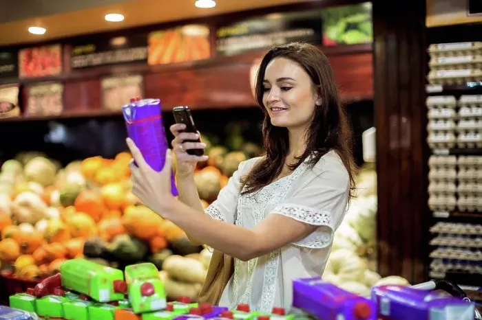Framed Print : Woman at supermarket scanning prices with her smart phone Framed Print : Woman at supermarket scanning prices with her smart phone