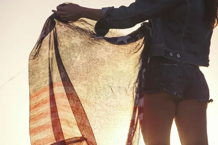 Framed Print : Woman wearing denim shorts, holding American flag, mid section, rear view