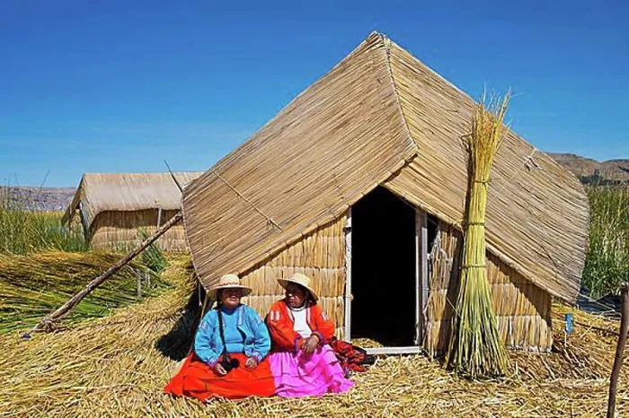 Framed Print : Two women of the Uro Indians wearing traditional dress sitting in front of a reed hut
