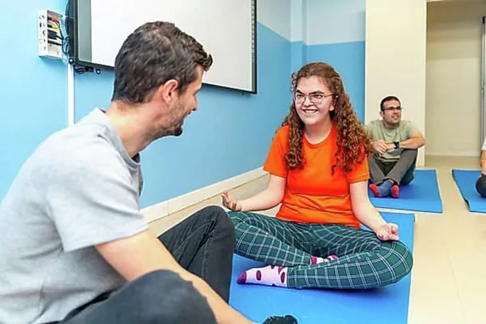 Framed Print : Yoga instructor and disabled woman talking while practicing yoga sitting on a mat with other people