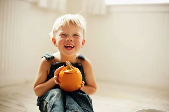 Framed Print : Young boy holds a small Jack O'Lantern on his knees as he sits on a floor and poses for a portrait Framed Print : Young boy holds a small Jack O'Lantern on his knees as he sits on a floor and poses for a portrait