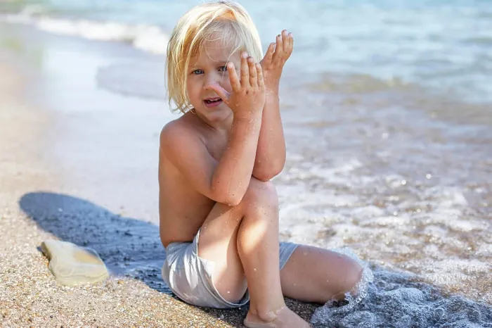 Framed Print : A young child sitting on a sandy beach covering one side of their face with sand-covered hands Framed Print : A young child sitting on a sandy beach covering one side of their face with sand-covered hands
